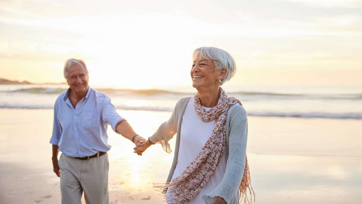 Image of an elderly couple holding hands on a beach.